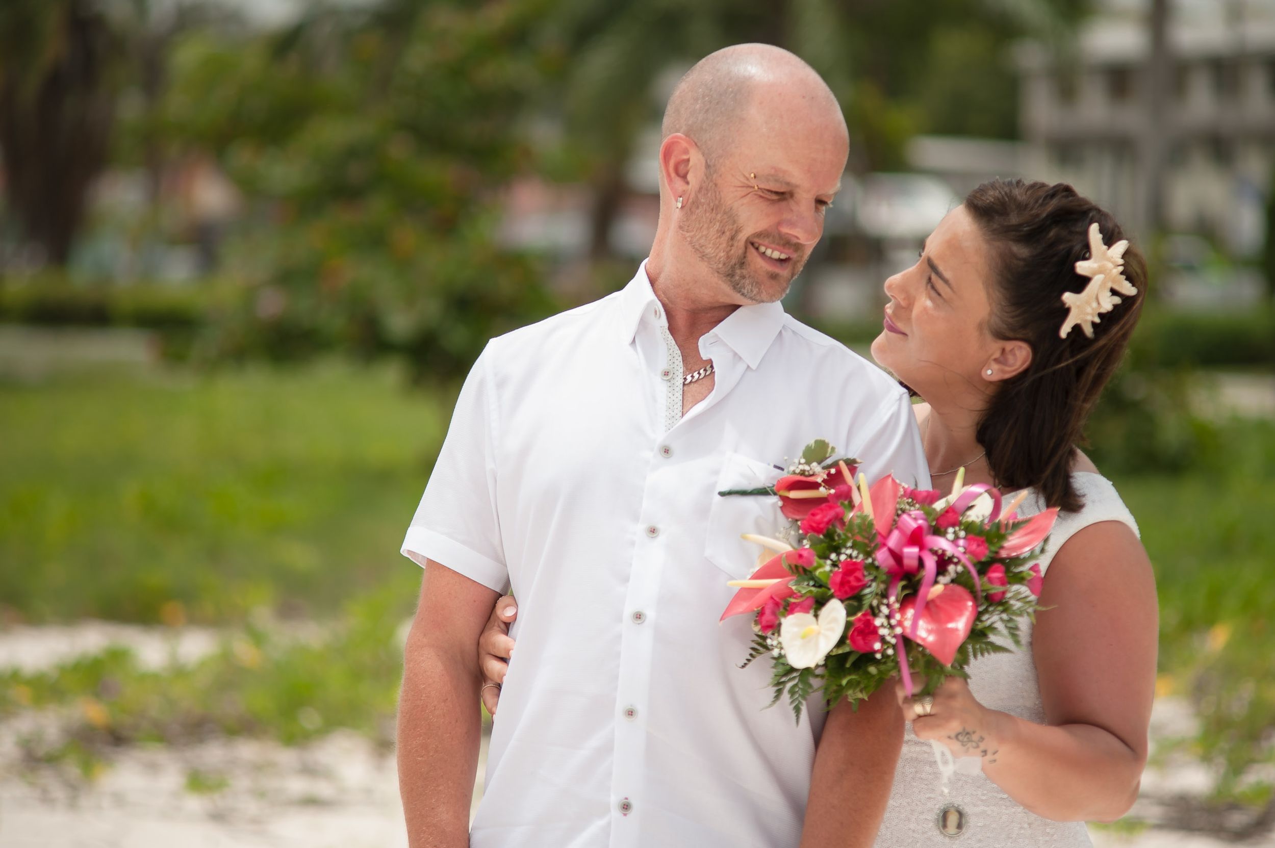 A happy couple shares a joyful moment at their beach wedding, with the bride holding a pink and white tropical bouquet.