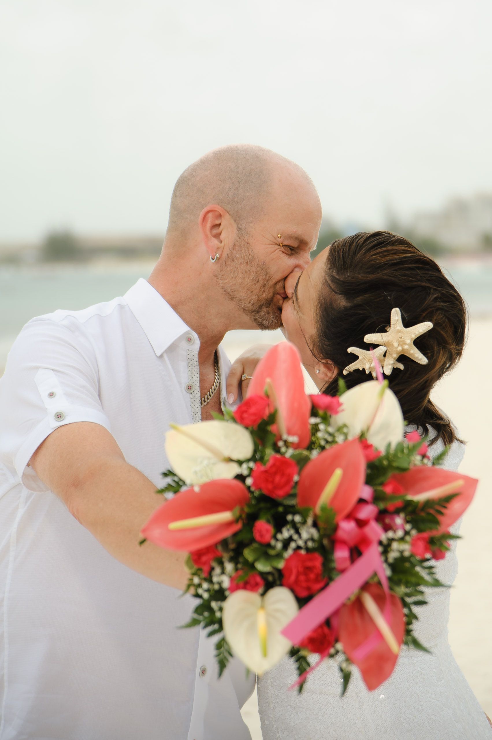 A romantic beach wedding moment with a beautiful tropical bouquet featuring red and white flowers with a starfish accent.