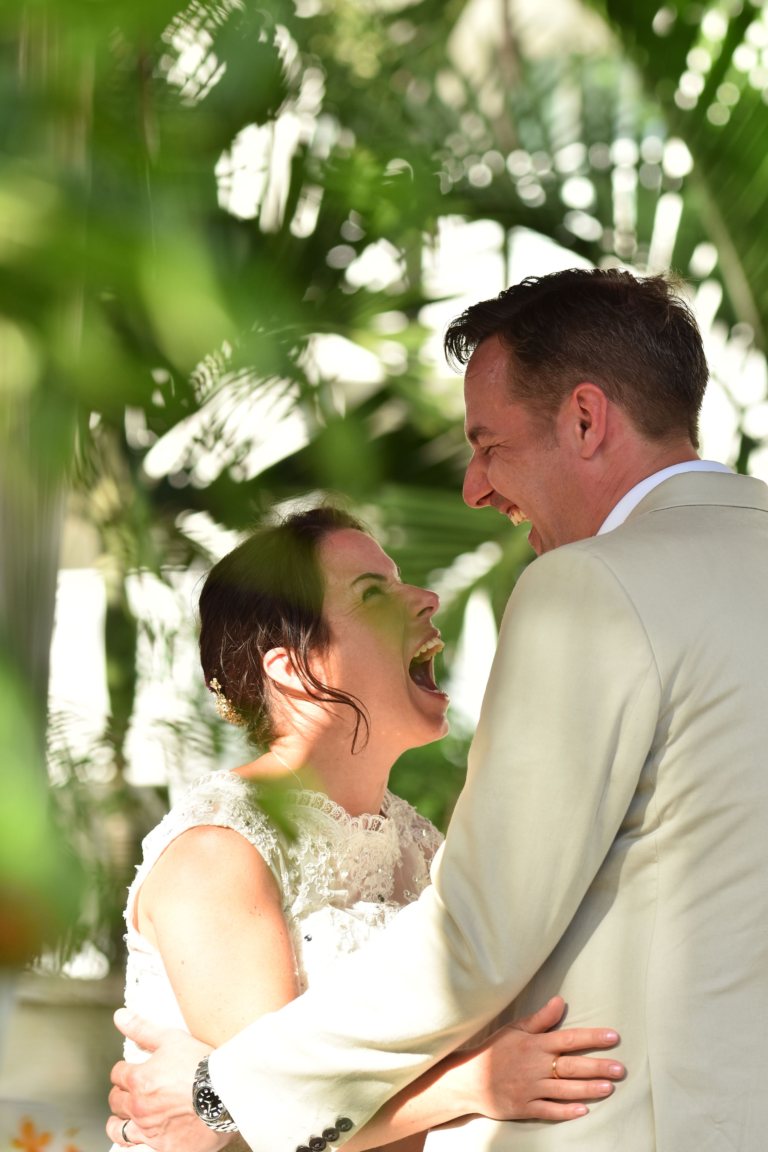 A couple shares a joyful moment together outdoors, with sunlight filtering through green foliage in the background.