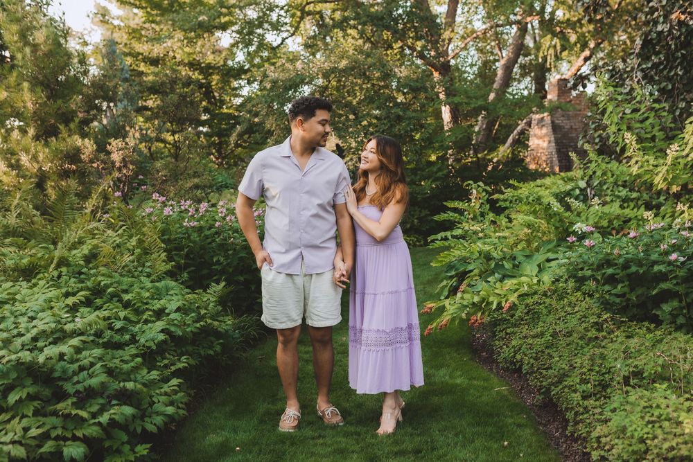 A happy couple standing together on a garden path surrounded by lush green foliage on a sunny day.
