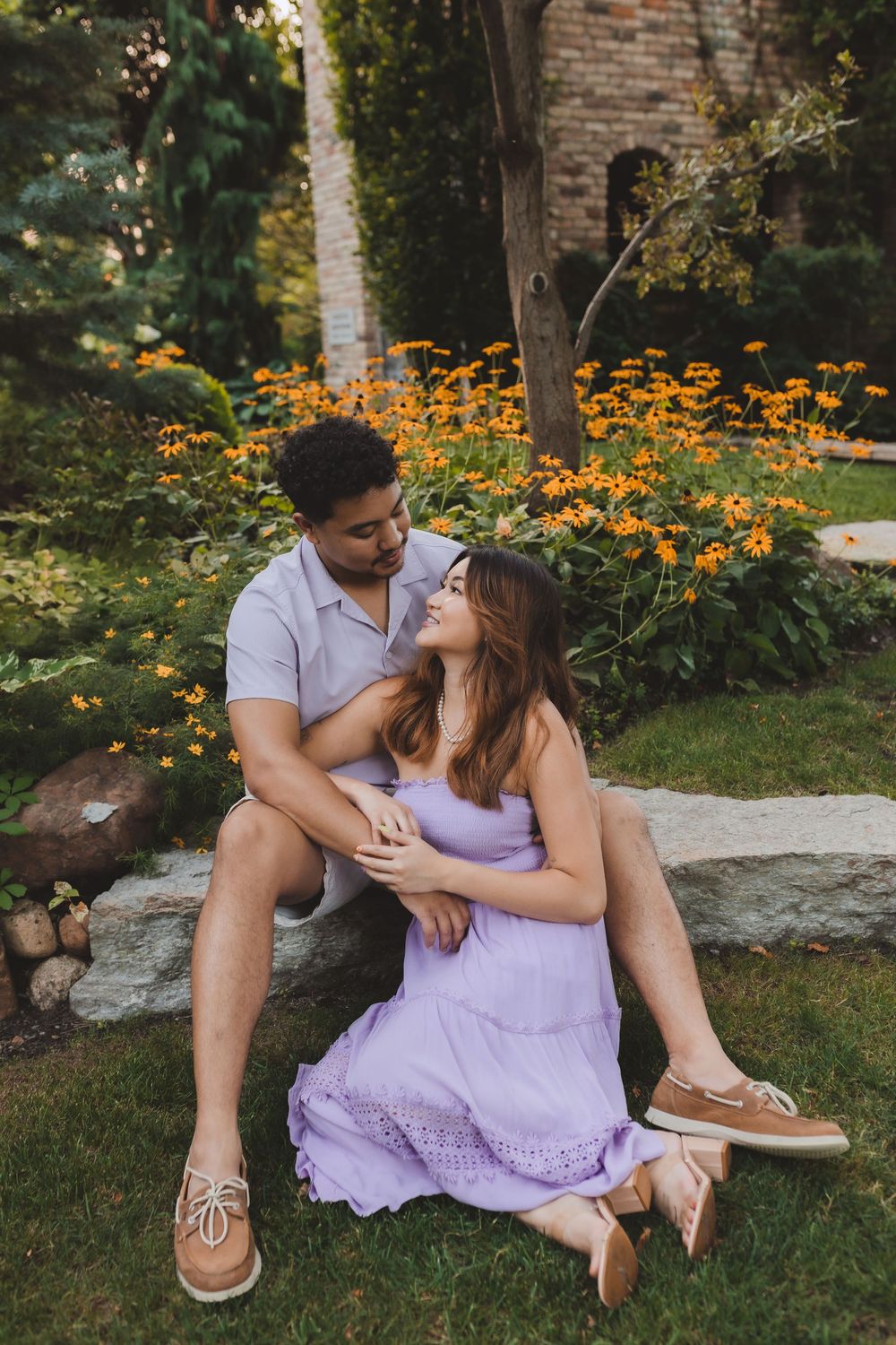 A couple sits together on stone steps surrounded by orange marigolds and greenery in a romantic garden setting.