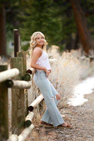 Country fashion portrait with light colored blouse and distressed flare jeans posed by wooden fence in outdoor setting.