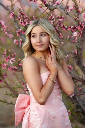 A spring portrait under blooming pink cherry blossoms with a strapless pink gown and delicate jewelry.