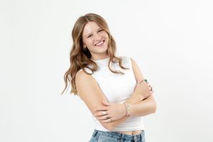 Woman in casual white top and jeans smiles while posing against white background in studio photos series.