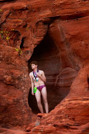 Person in bikini standing in a red sandstone cave formation in a desert landscape.
