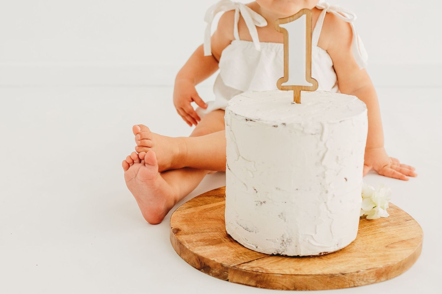 A white birthday cake with a gold number one topper sits on a wooden board.