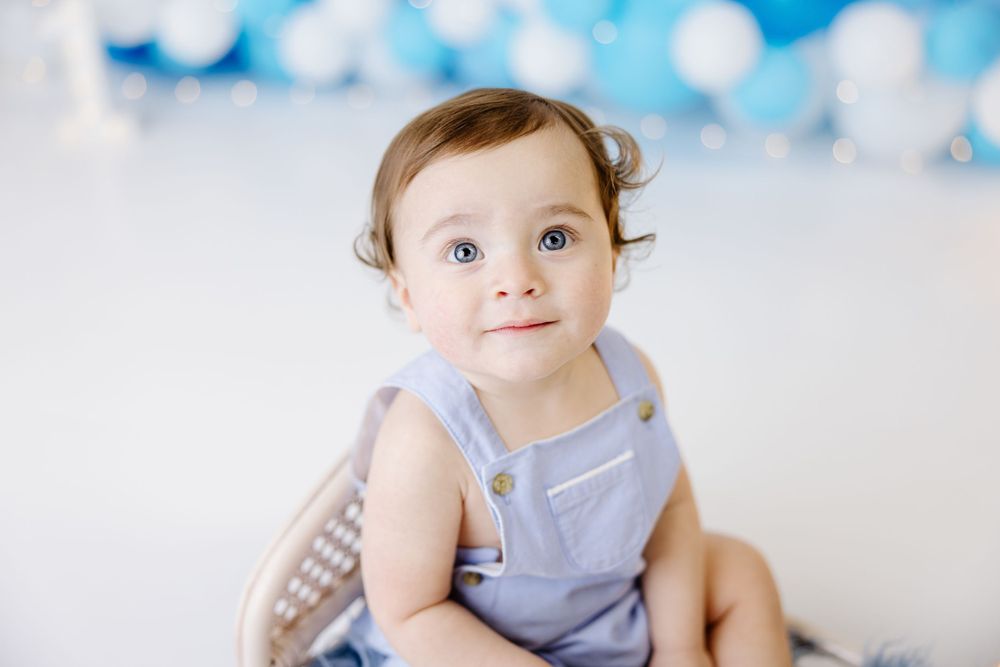 A baby wearing blue outfit sits against a backdrop with blue bokeh effects.