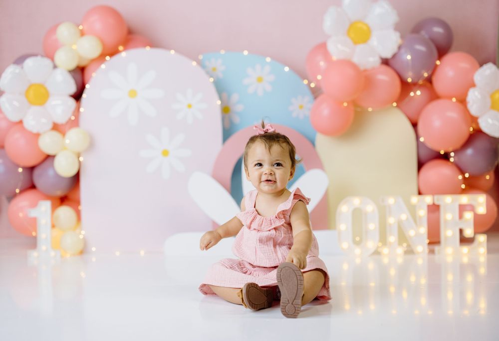 Birthday setup with pink and blue balloons, floral decorations and illuminated ONE sign.