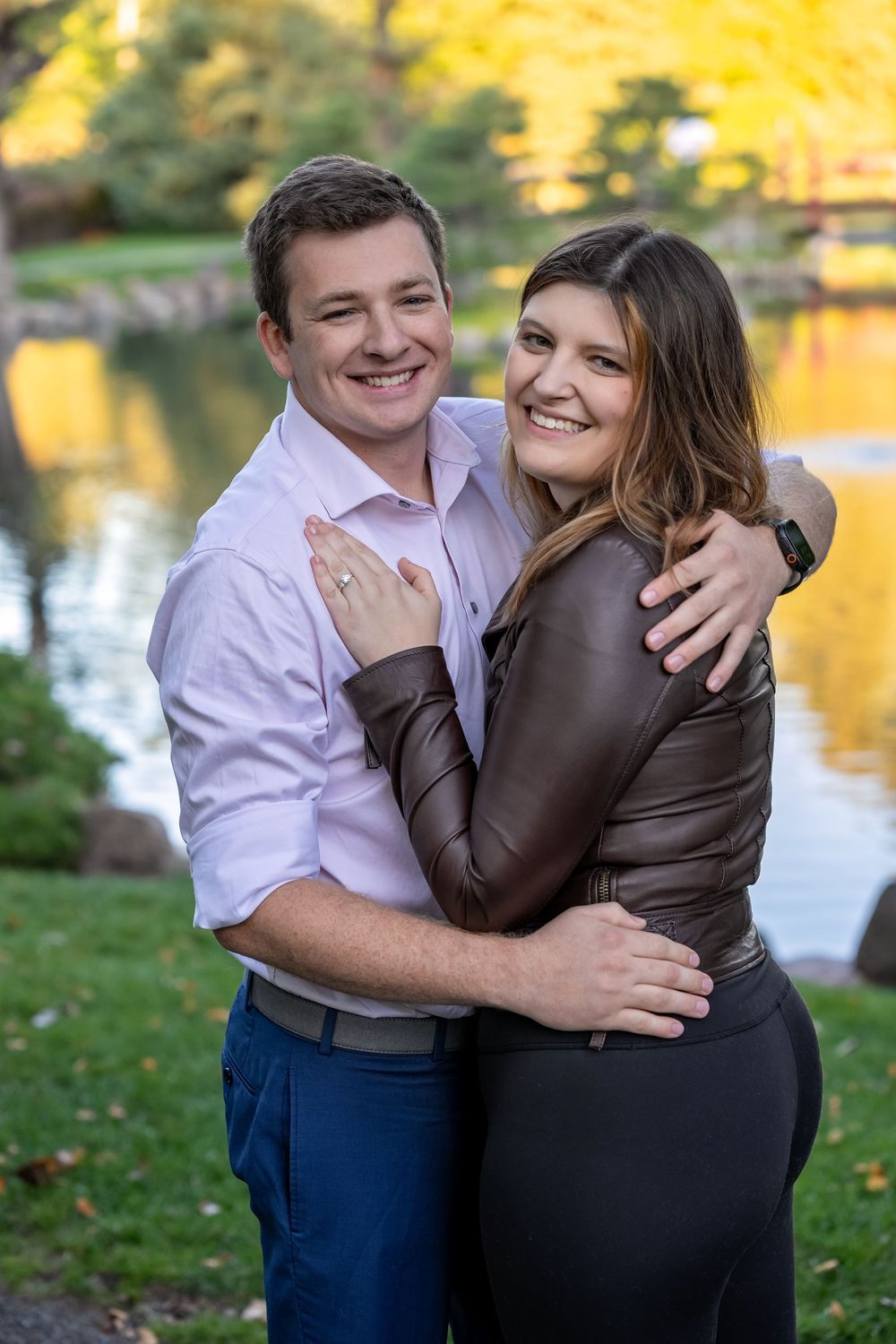Happy engaged couple embracing and smiling beside autumn park pond.