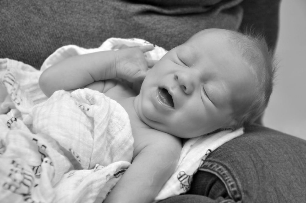 Black and white photo of baby yawning while lying on soft surface.