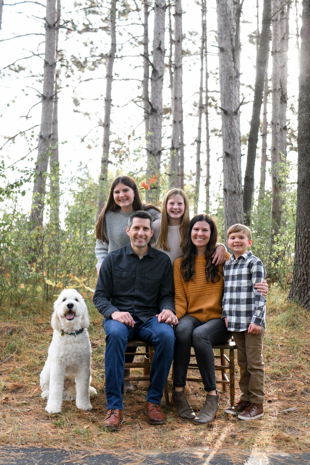 Family and pet dog sitting on wooden bench in pine forest setting.