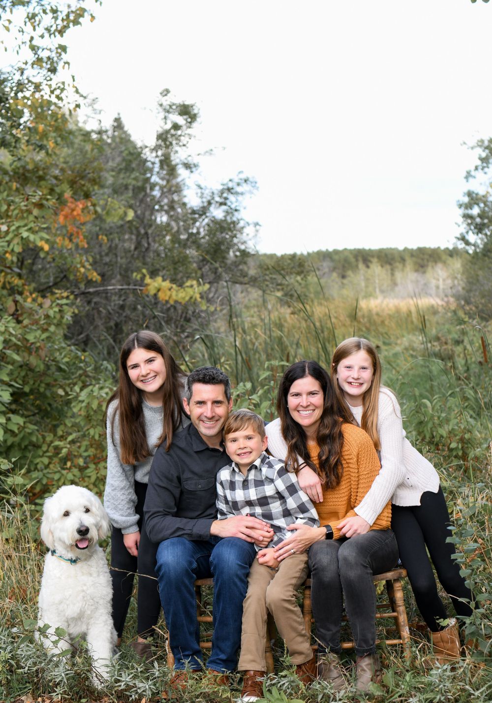 Happy family and their white dog enjoying a sunny fall day in a field.