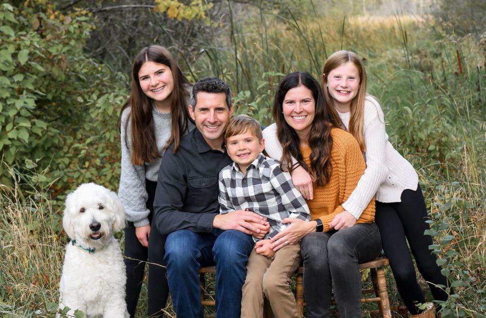 Family portrait outdoors with a white dog sitting together on fallen leaves.