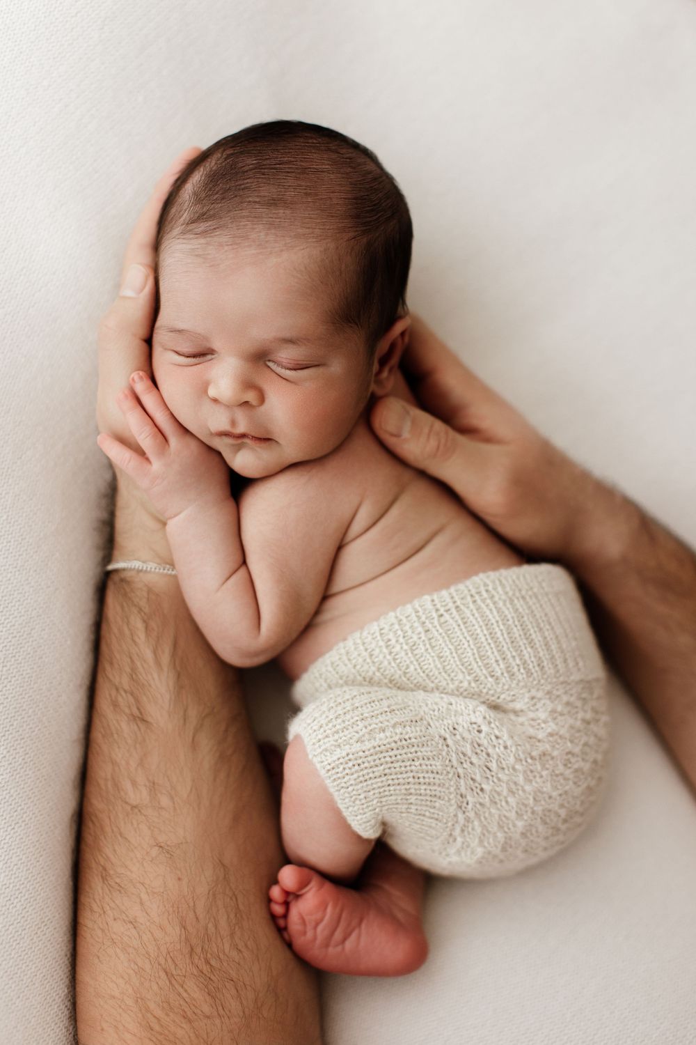 Natural light newborn photo in father's arms with cream bloomers in Mesa AZ by Jen Roberts Photographer
