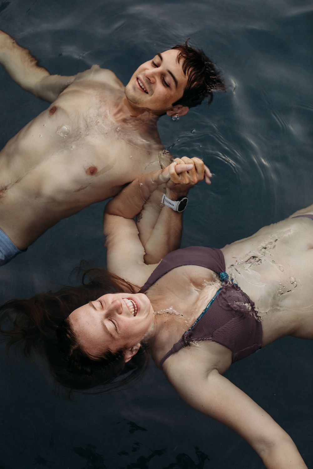 Two people float peacefully in blue pool water on a sunny day.