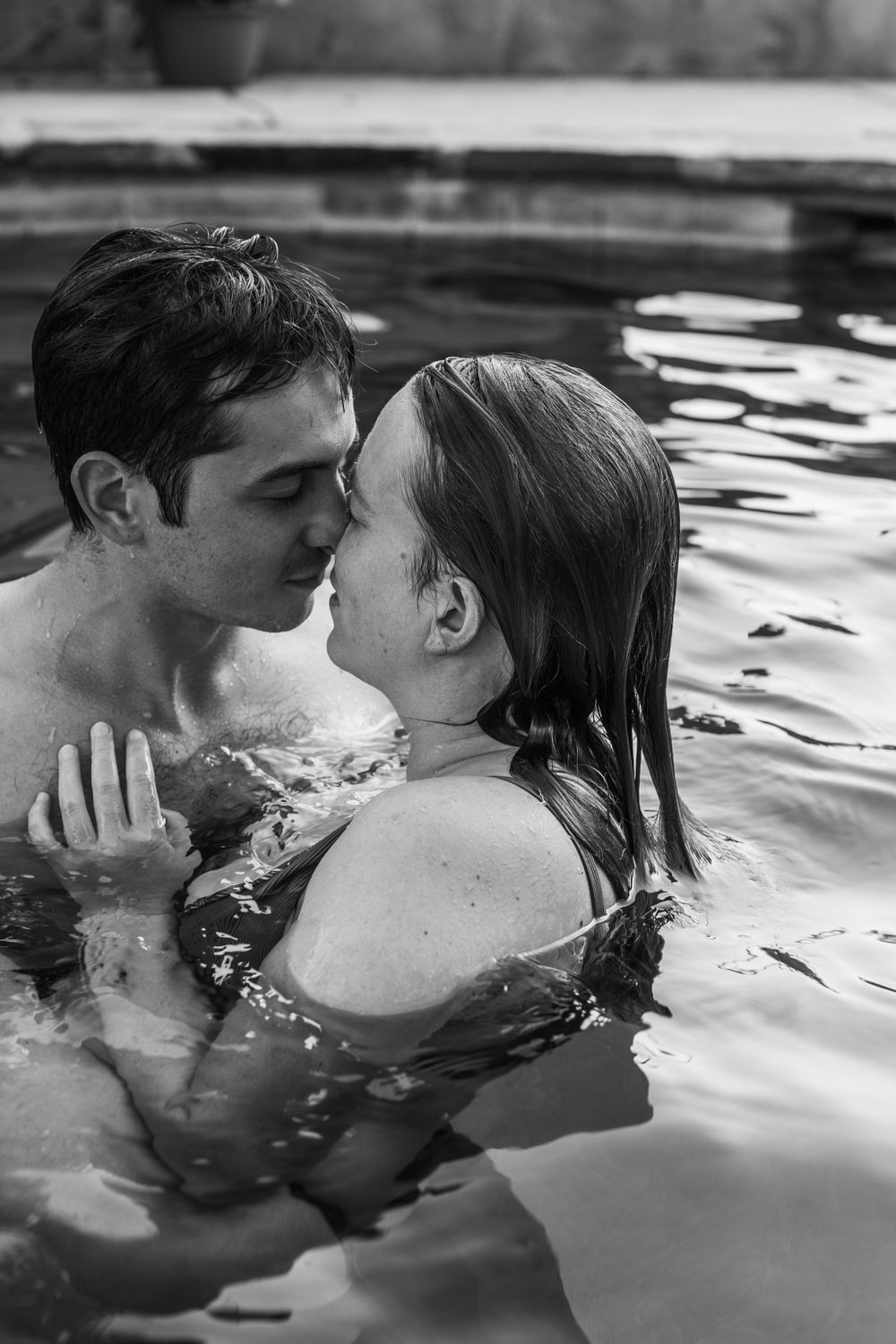 A romantic couple shares an intimate kiss while swimming in dark rippling water.