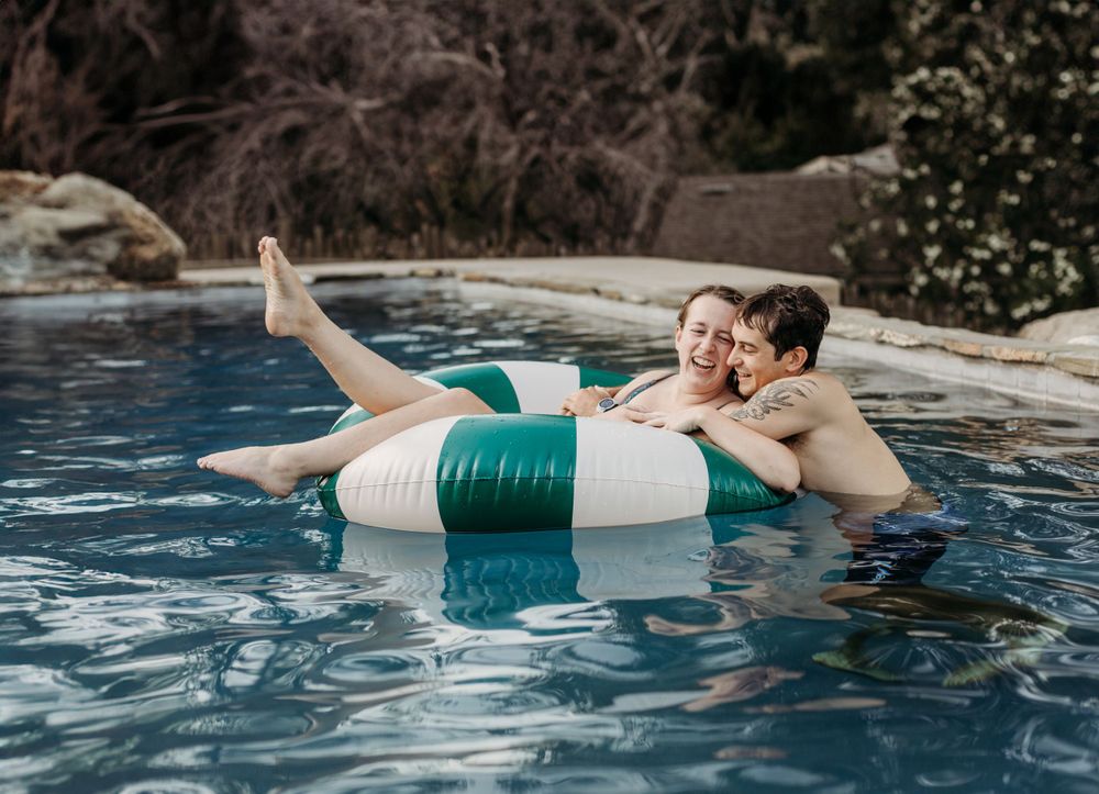 Couple relaxing together on a green and white pool float in a swimming pool.