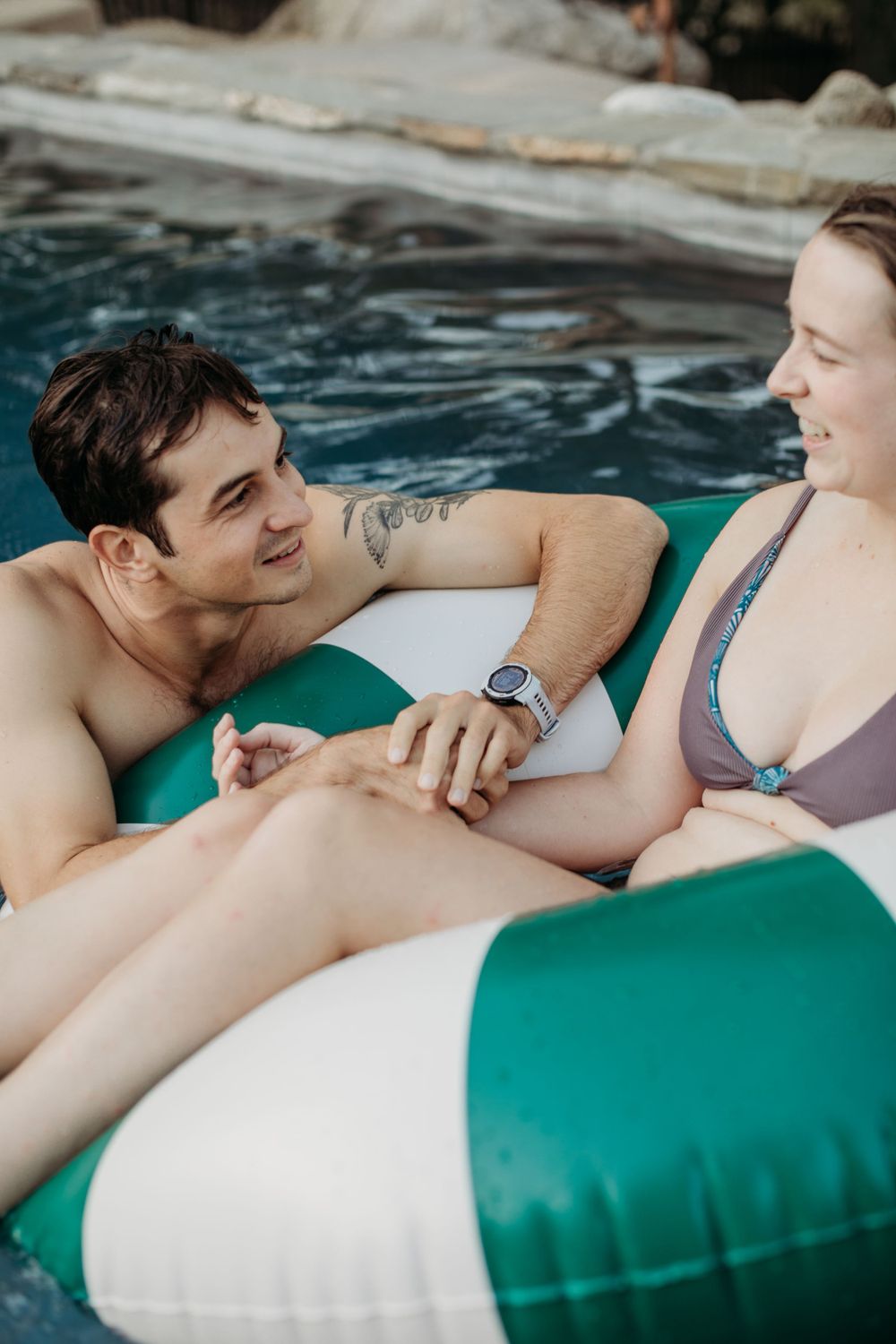 Happy couple lounging on inflatable pool float sharing intimate moment.