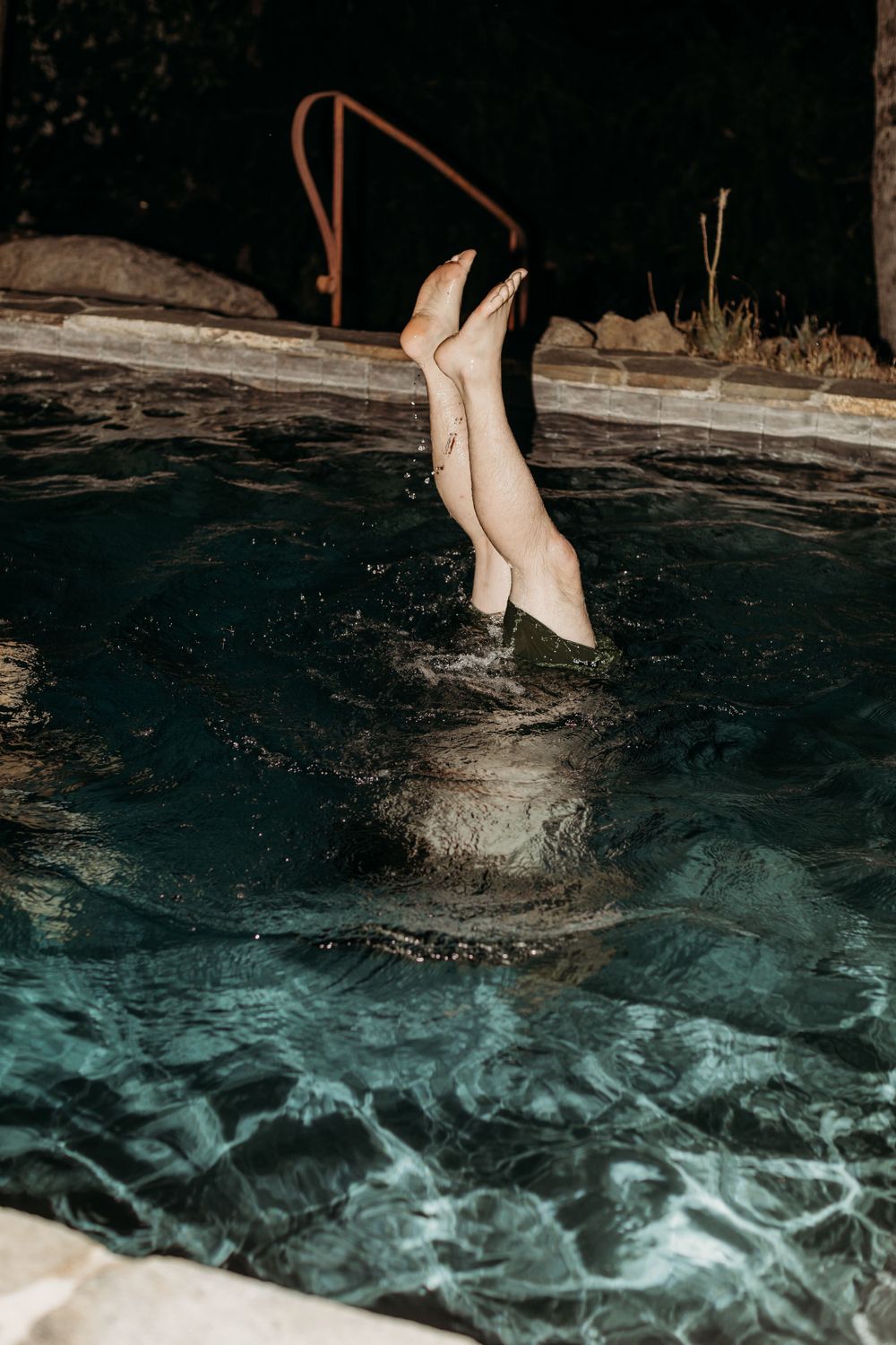 Legs emerge from a dark swimming pool creating a playful splash at night.