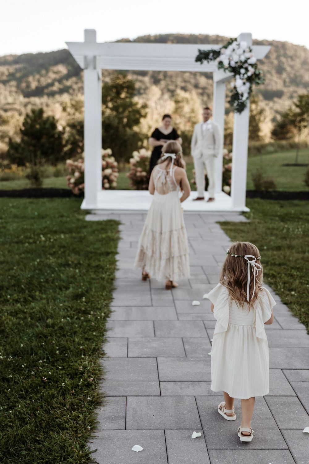 A series of photos showing a child in a white dress walking away on a stone path surrounded by white pillars and greenery.