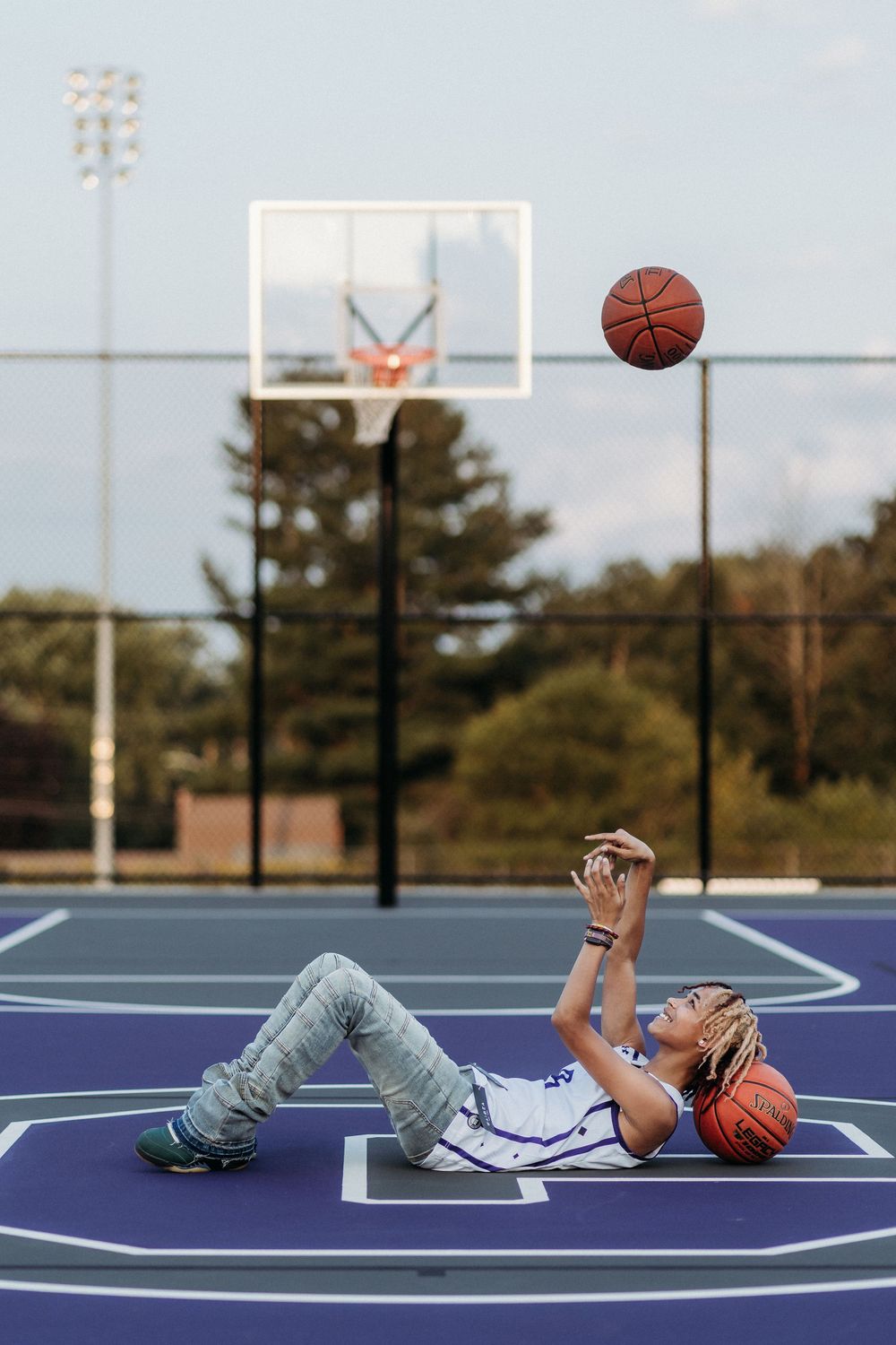Basketball player lying on blue court tossing ball in air in sequence of three connected photos.