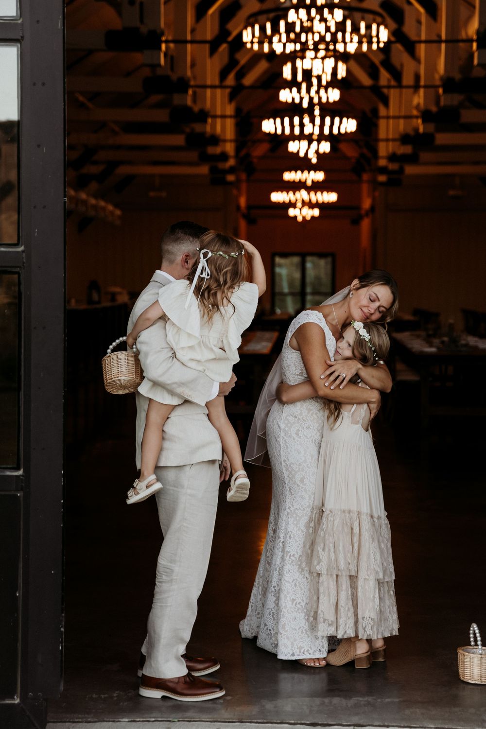 Intimate candid moments between wedding party members sharing embraces in an elegant venue with crystal chandeliers.