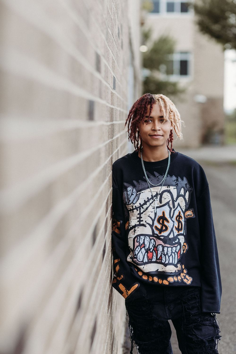 A person in a black graphic t-shirt poses against a white wall in an artistic portrait series.