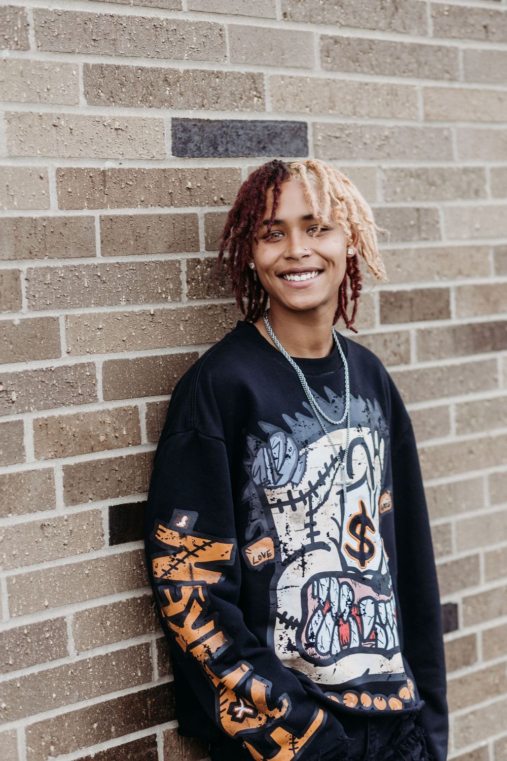 A person wearing a black graphic sweatshirt poses against a brick wall in a series of casual shots.