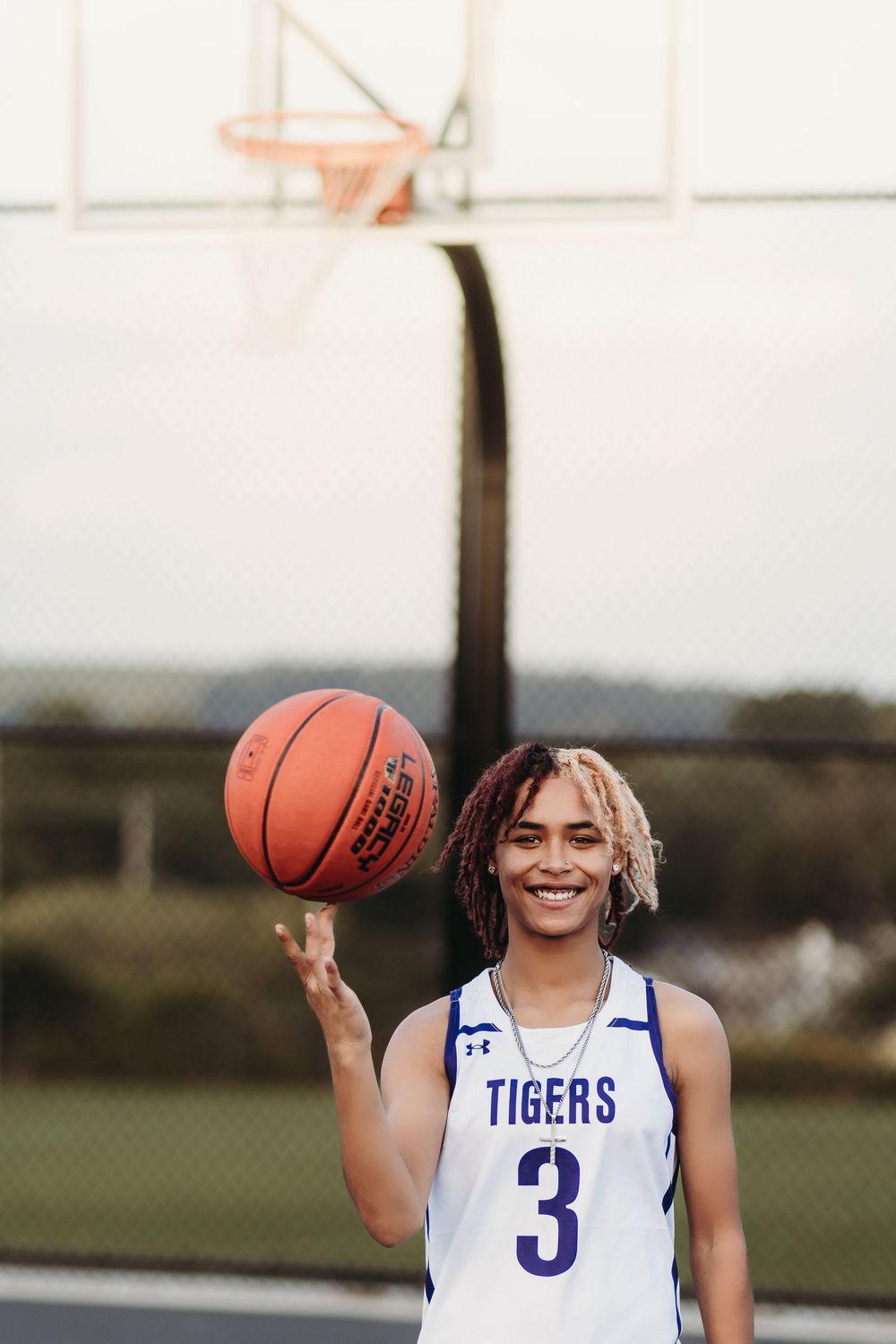 Basketball player in blue and white Tigers jersey number 3 holds ball while posing outdoors.