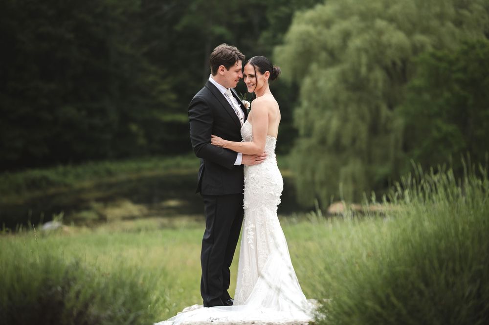 Wedding couple's romantic embrace on a grassy hilltop with lake and willow at The Ruins at Sassafras in New Lebanon NY Hudson Valley