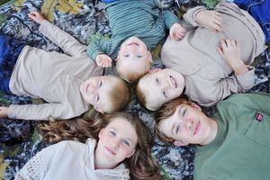 Group of children lying in circle on blanket with heads together.