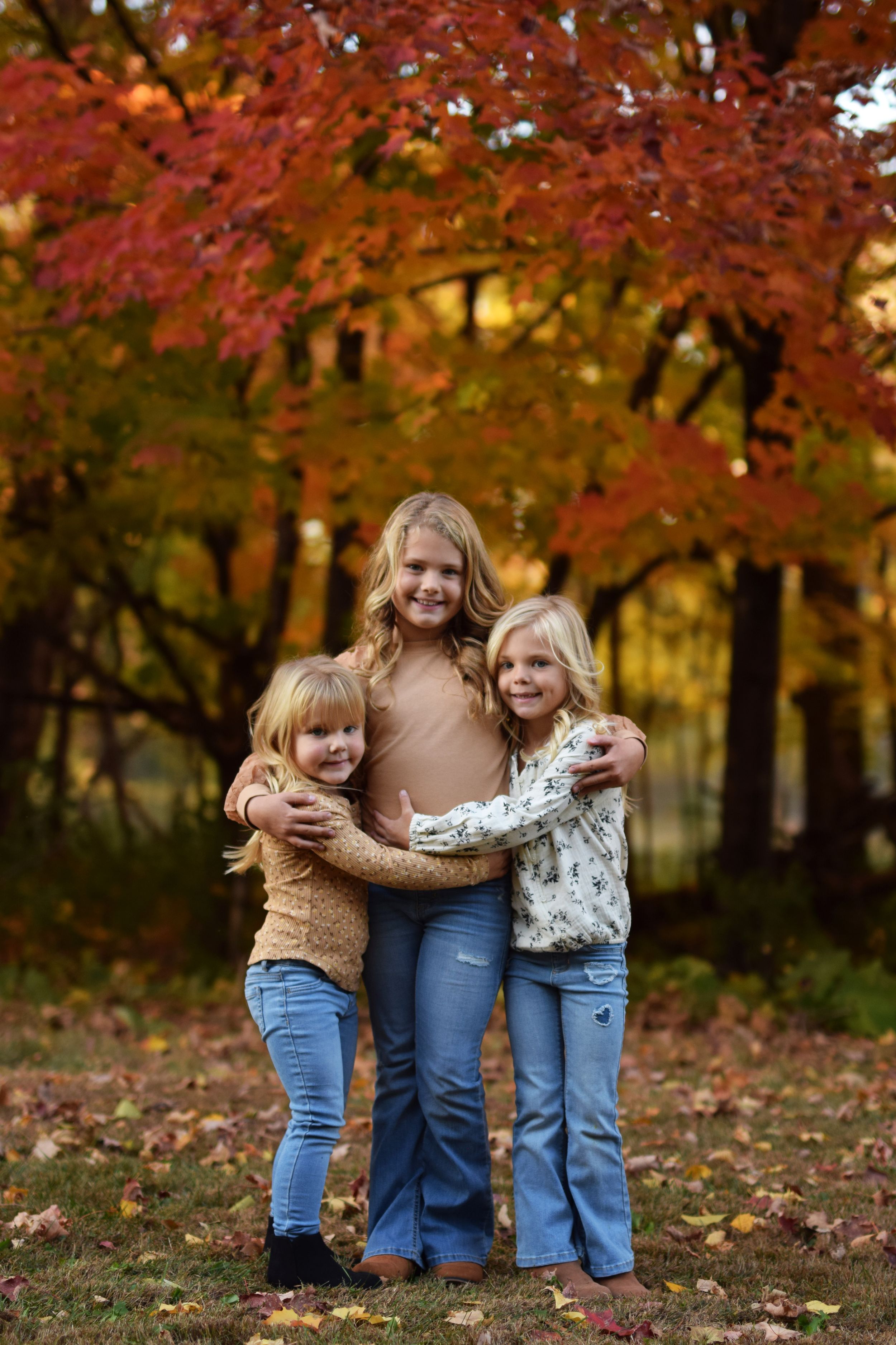 Family group poses together under vibrant red autumn maple trees.