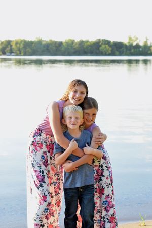 Children embrace while posing for photo by lakeside in summer clothing.