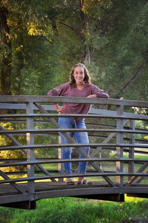 Person in casual attire poses playfully on wooden bridge in park setting.
