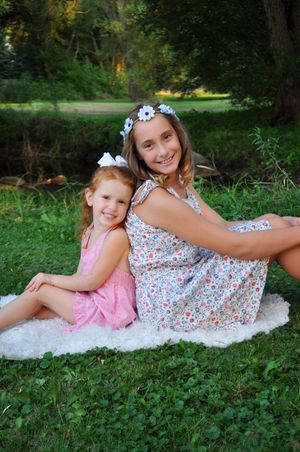 Two people in floral dresses pose on white blanket in green grass during summer photoshoot.