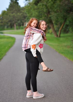 Playful piggyback ride on paved path surrounded by green trees.