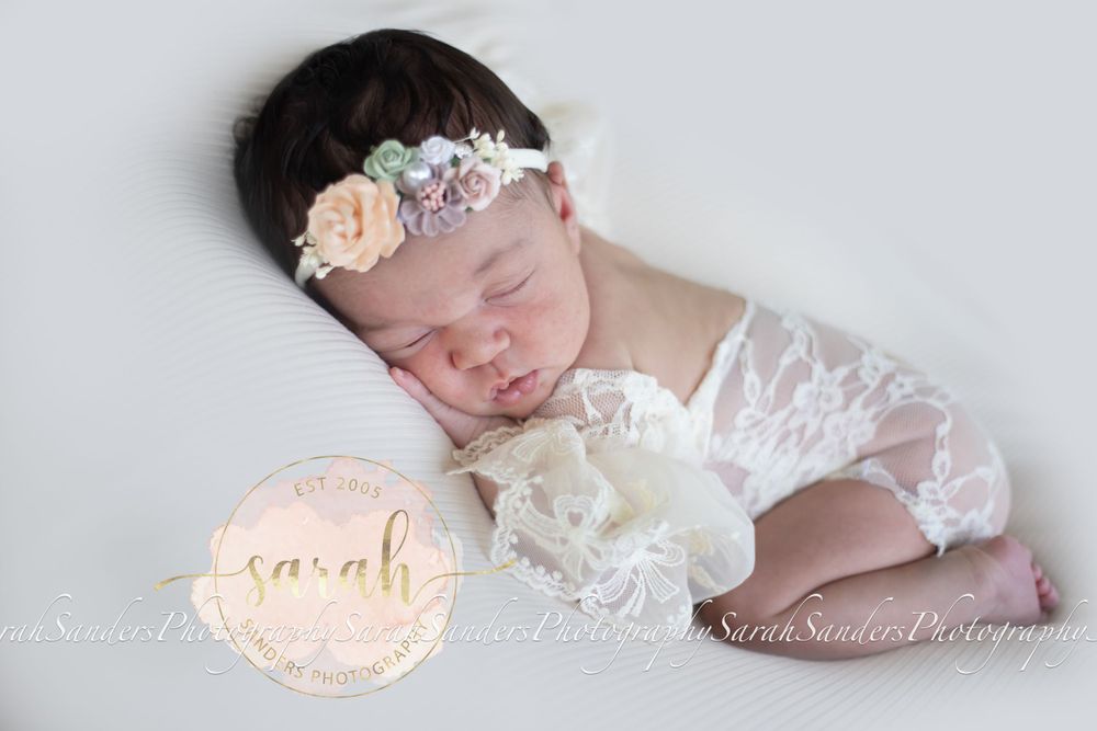 Newborn on belly side posed in lace romper with floral headband