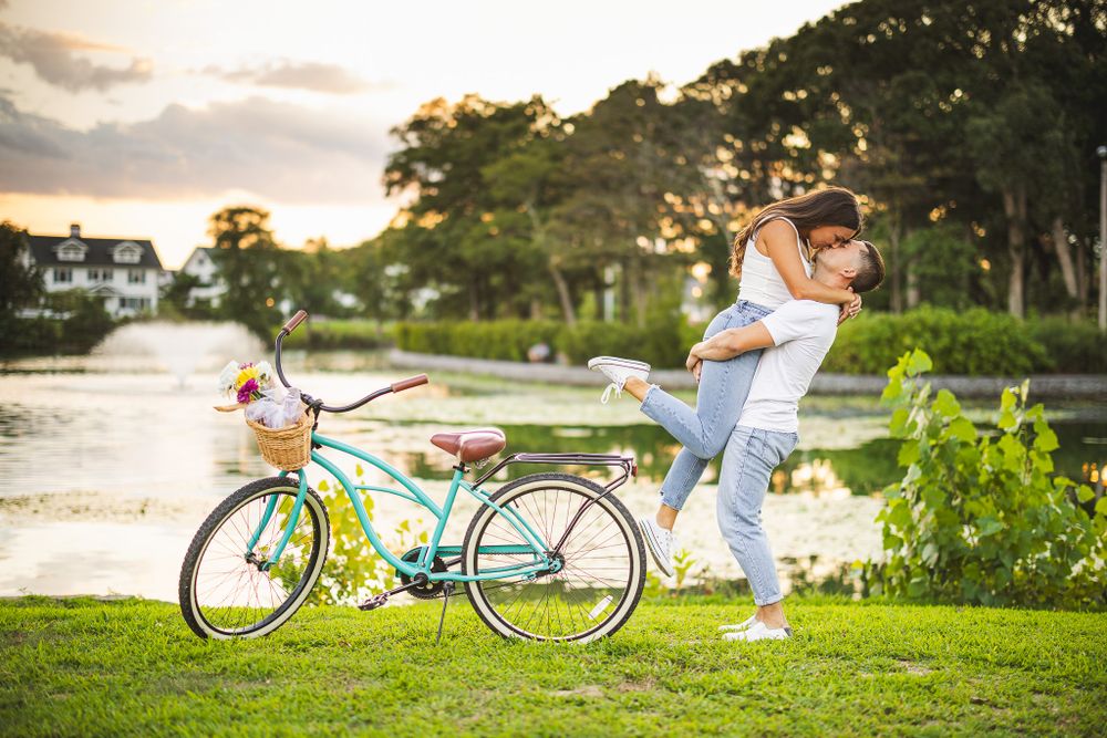 engaged couple lifted and kissing next to beach bike in spring lake