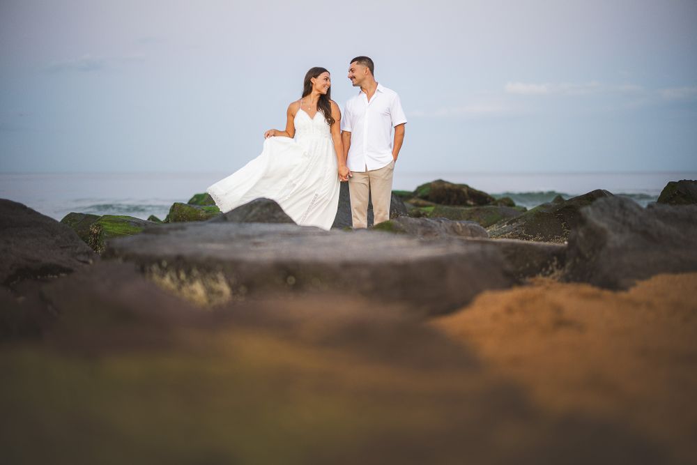 engaged couple standing on jetty holding dress to side smiling at each other in spring lake