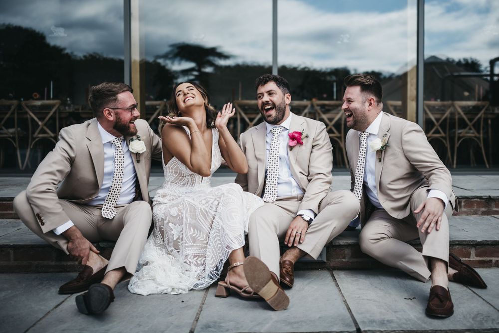 bride, groom and best men sat on steps at Thorpe Garden laughing