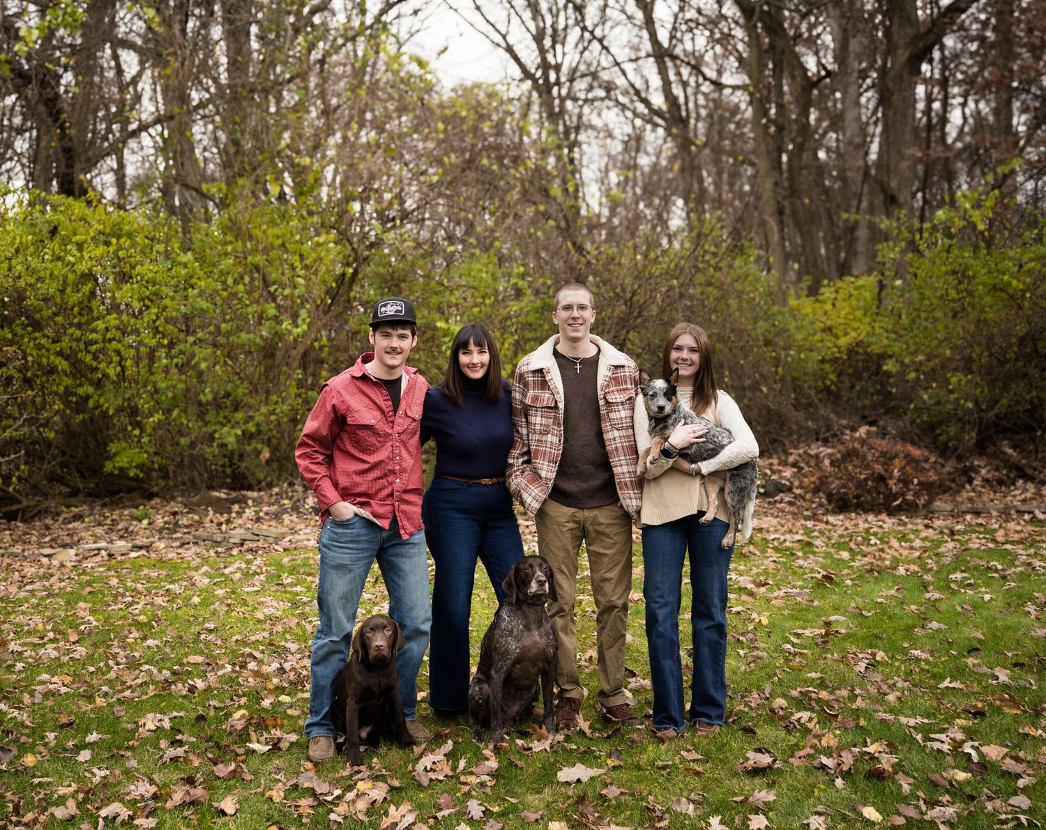 Group of friends in casual fall attire pose together against dark foliage background.