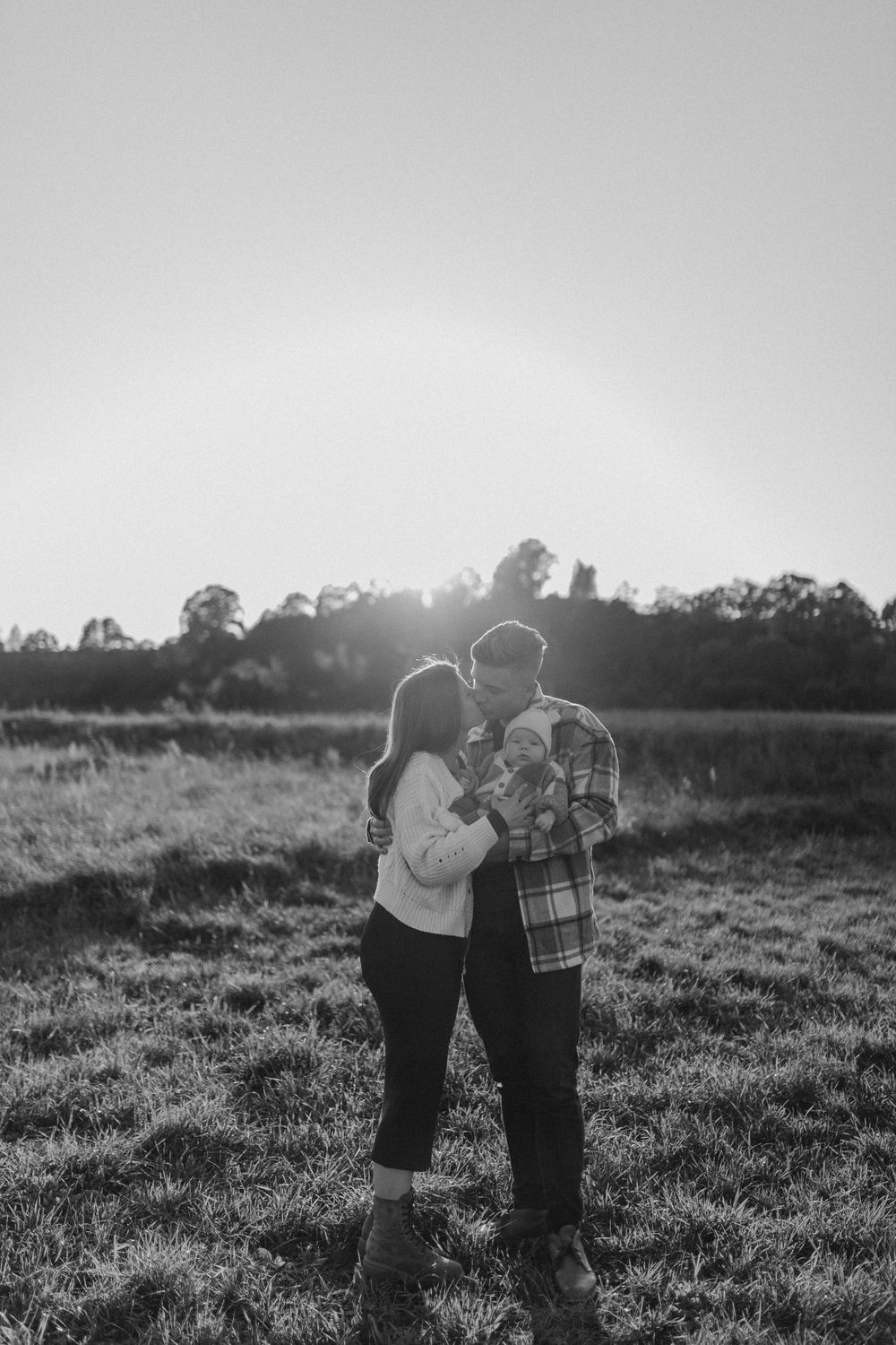 Two people sharing an intimate moment in a sunlit field at dusk.