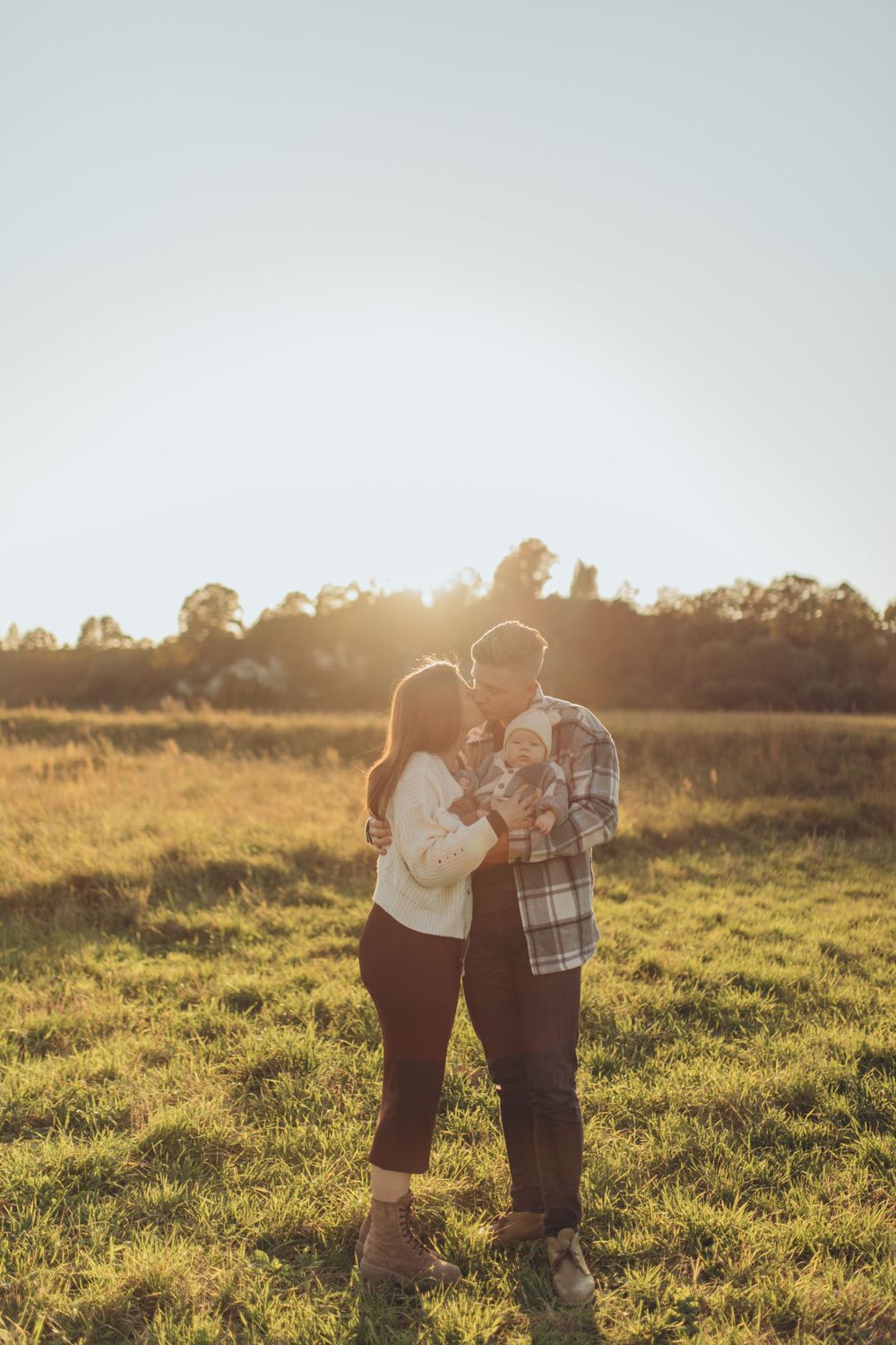 A couple embraces in a golden sunlit field during sunset.