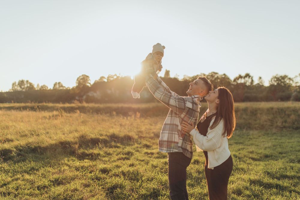 Parents playfully lift their small child in the air on a sunny field.