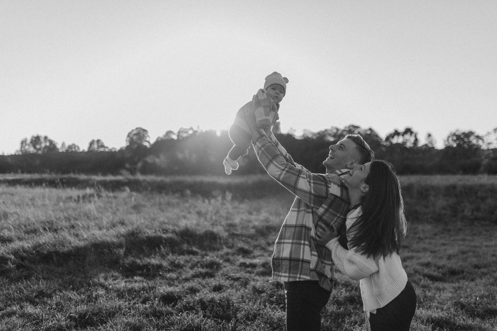 Black and white capture of parents lifting their child in a meadow.