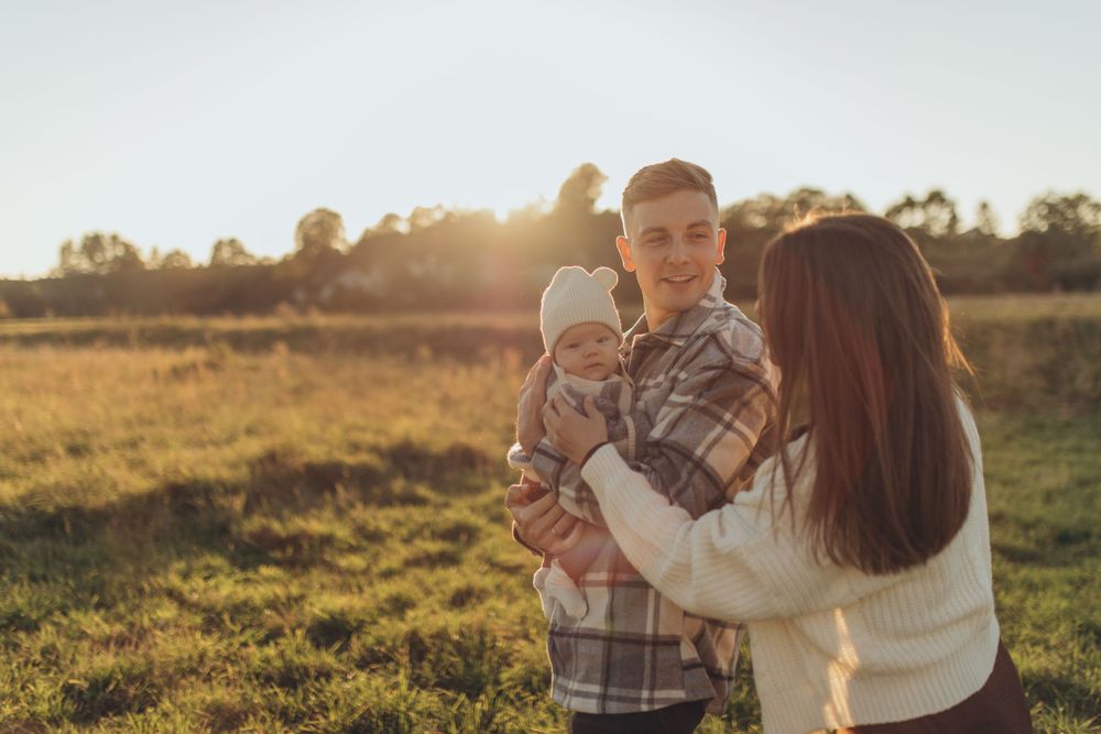 Family shares tender moment together in sunlit field during golden hour.