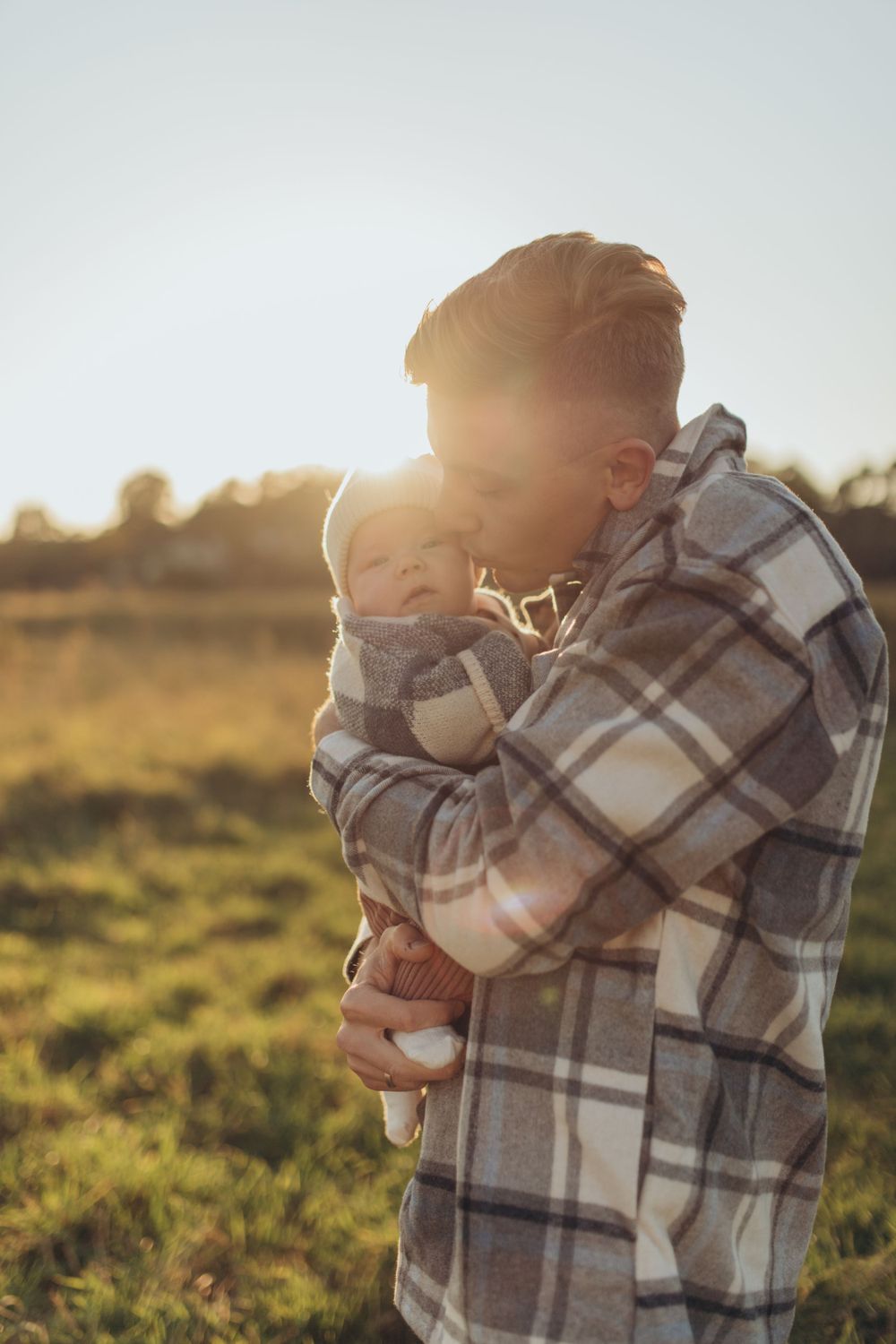 Silhouette of parent holding baby against sunset in grassy field.