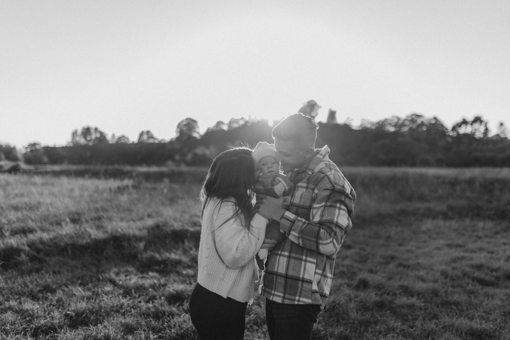 A couple shares an intimate moment in a sunlit field during sunset, captured in black and white.
