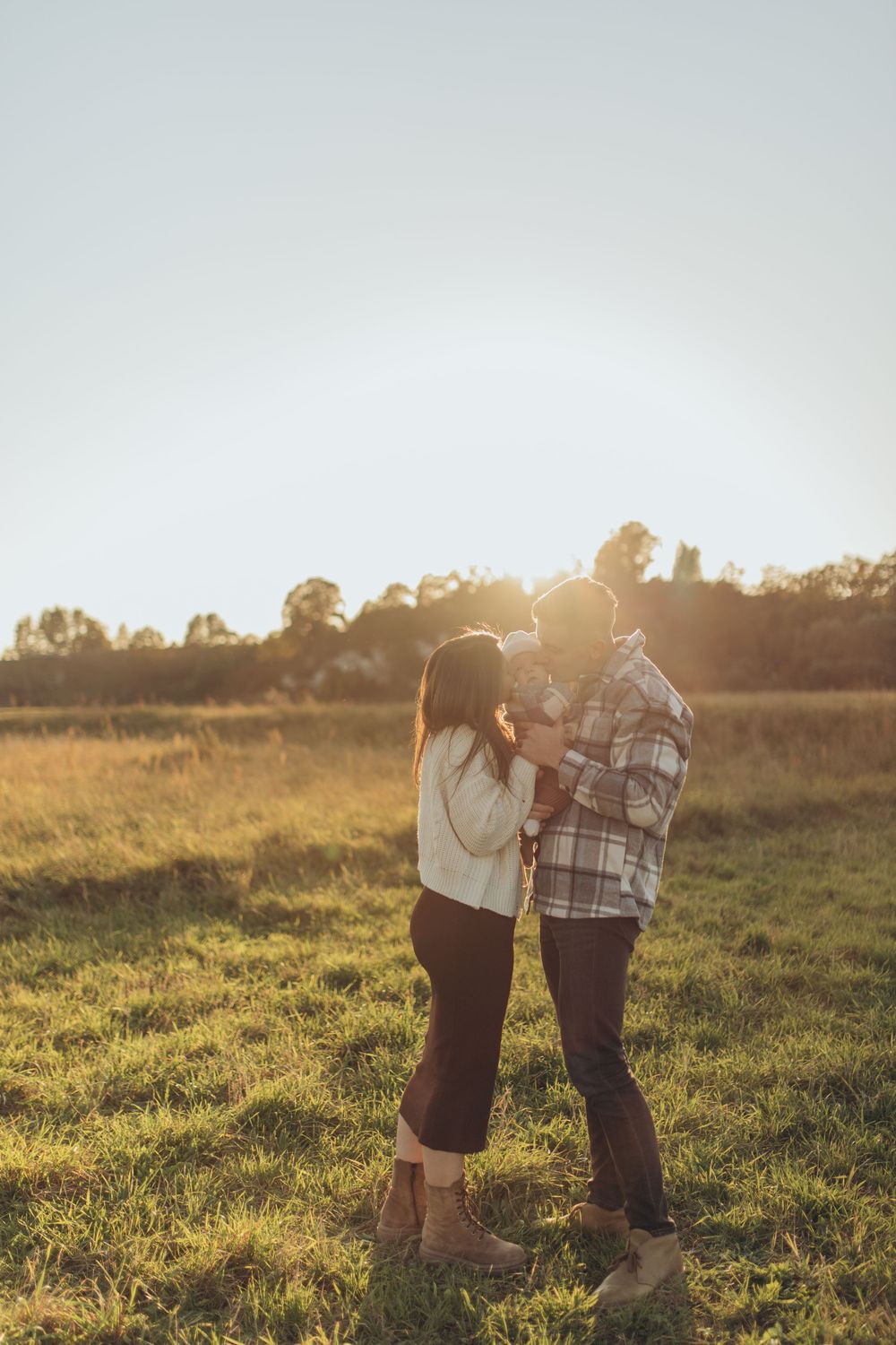 A tender moment between two people backlit by warm late afternoon sunlight in a grassy field.