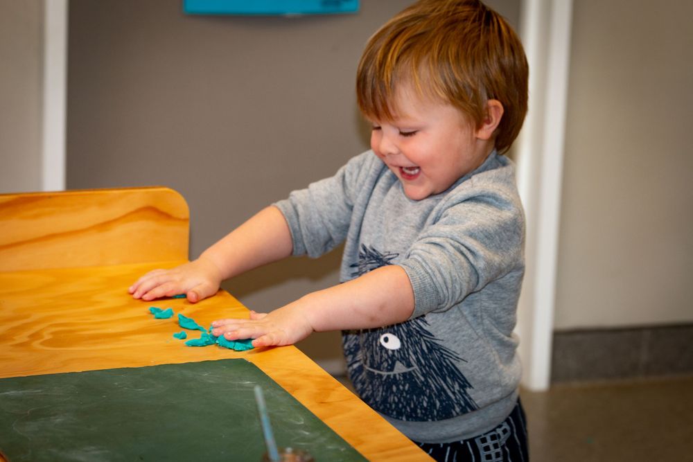 A toddler plays with colorful items on a wooden table surface.